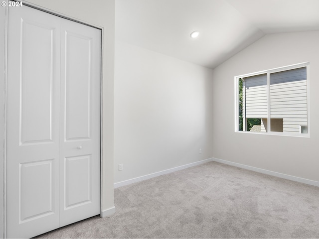 unfurnished bedroom with a closet, light colored carpet, and vaulted ceiling