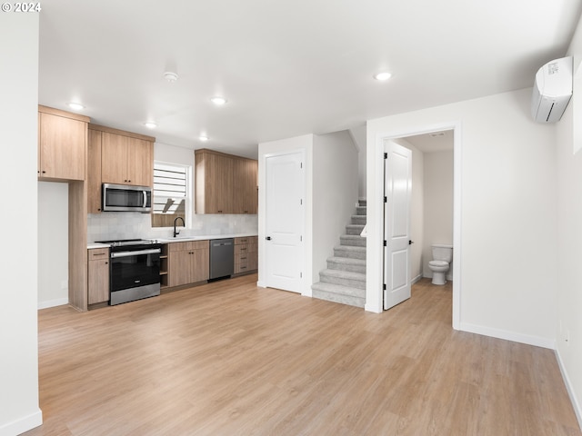 kitchen with backsplash, an AC wall unit, sink, light wood-type flooring, and appliances with stainless steel finishes