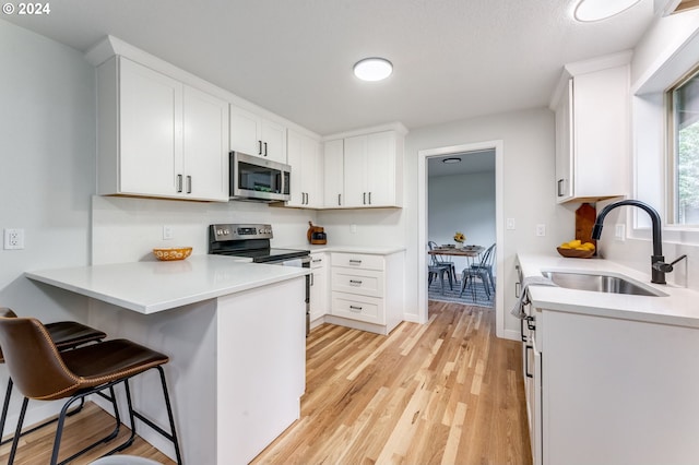 kitchen with sink, light wood-type flooring, appliances with stainless steel finishes, and white cabinetry