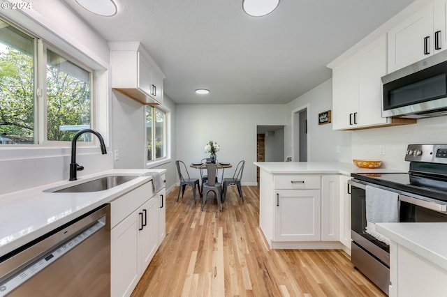 kitchen featuring kitchen peninsula, light hardwood / wood-style flooring, white cabinets, appliances with stainless steel finishes, and sink