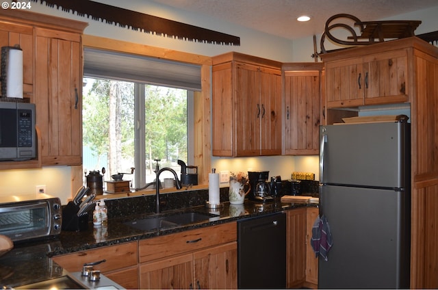 kitchen with dark stone countertops, a textured ceiling, stainless steel appliances, and sink