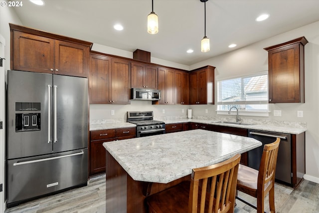 kitchen featuring appliances with stainless steel finishes, sink, pendant lighting, light hardwood / wood-style flooring, and a kitchen island