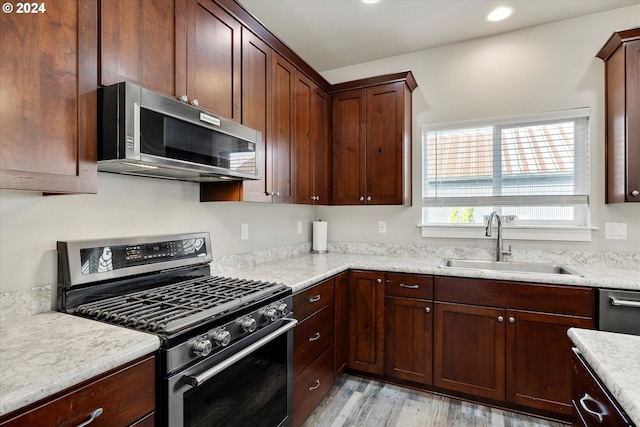 kitchen with light stone counters, sink, light wood-type flooring, and appliances with stainless steel finishes