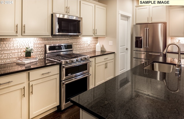 kitchen featuring sink, stainless steel appliances, dark hardwood / wood-style floors, dark stone countertops, and cream cabinetry