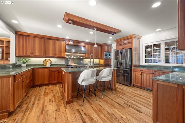 kitchen with a breakfast bar area, decorative light fixtures, an island with sink, stainless steel appliances, and wall chimney range hood