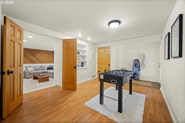 game room with built in shelves, wood-type flooring, and a textured ceiling