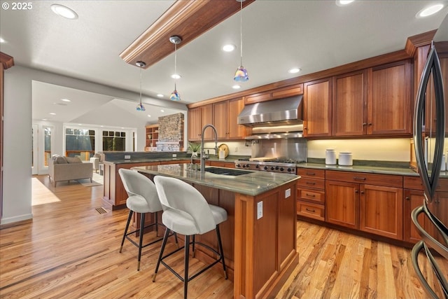 kitchen featuring refrigerator, decorative light fixtures, sink, a kitchen island with sink, and wall chimney range hood