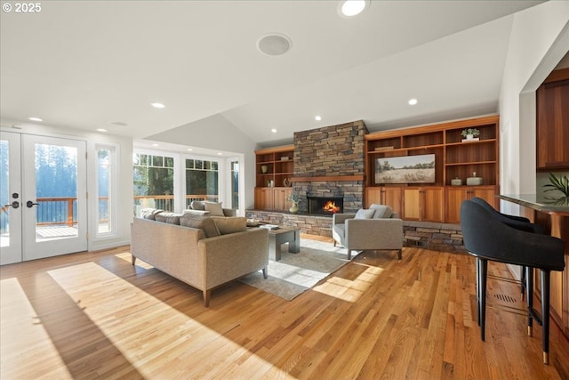 living room with a stone fireplace, vaulted ceiling, french doors, and light wood-type flooring