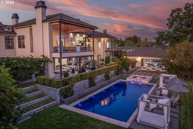 pool at dusk featuring an in ground hot tub and a patio area