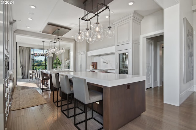 kitchen with white cabinets, custom exhaust hood, a large island, decorative light fixtures, and dark hardwood / wood-style flooring