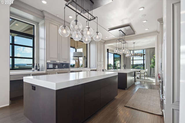 kitchen with pendant lighting, an island with sink, a chandelier, dark wood-type flooring, and appliances with stainless steel finishes