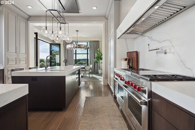 kitchen with dark hardwood / wood-style flooring, ventilation hood, decorative light fixtures, double oven range, and a kitchen island with sink