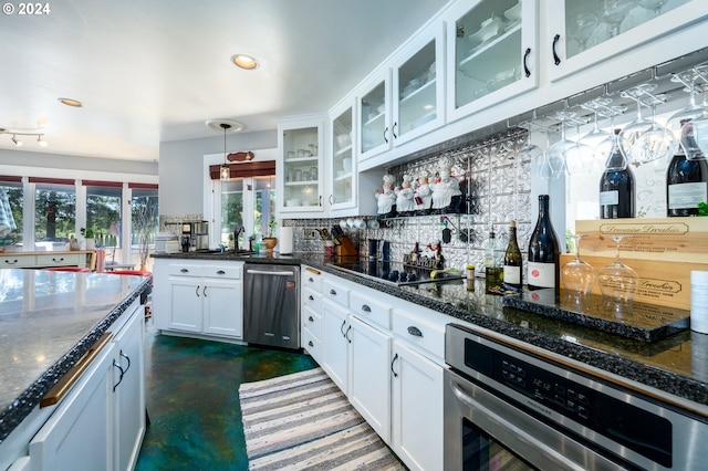 kitchen featuring backsplash, appliances with stainless steel finishes, hanging light fixtures, dark stone countertops, and white cabinets