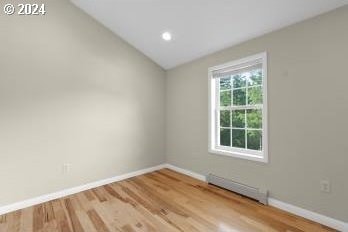 spare room with hardwood / wood-style floors, a baseboard heating unit, and vaulted ceiling