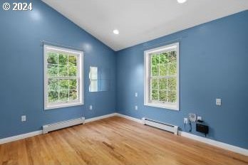 empty room with hardwood / wood-style floors, a baseboard radiator, and a wealth of natural light