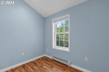 unfurnished room with vaulted ceiling, hardwood / wood-style flooring, and a baseboard heating unit