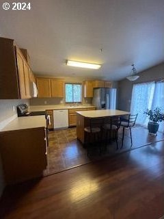 kitchen featuring dark wood-type flooring, white dishwasher, a center island, decorative light fixtures, and stainless steel fridge