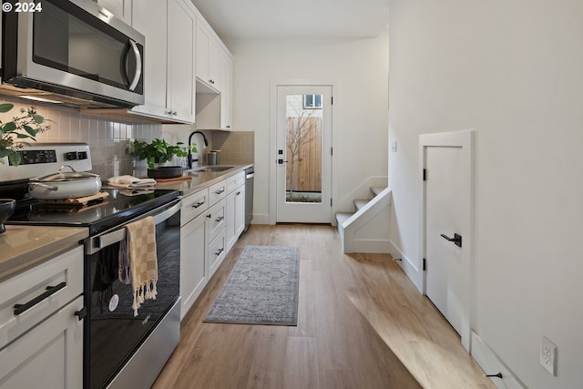 kitchen with sink, light hardwood / wood-style flooring, backsplash, white cabinets, and appliances with stainless steel finishes