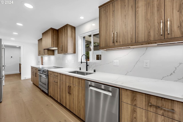 kitchen featuring tasteful backsplash, light stone countertops, stainless steel appliances, light hardwood / wood-style flooring, and sink