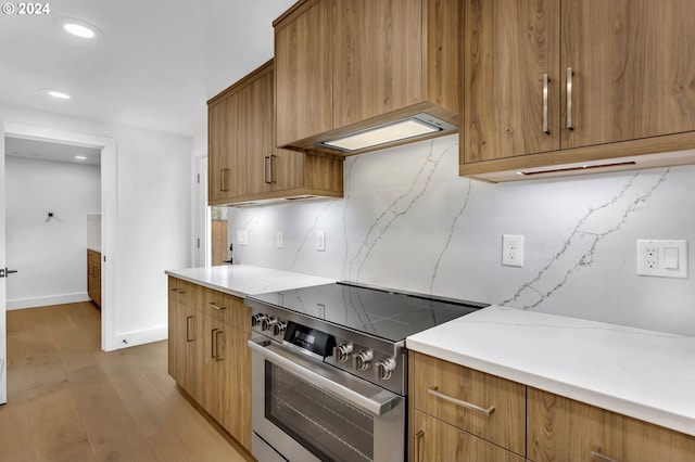 kitchen with stainless steel range, light wood-type flooring, extractor fan, and tasteful backsplash