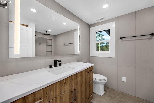 bathroom with tile walls, vanity, toilet, and tile patterned floors