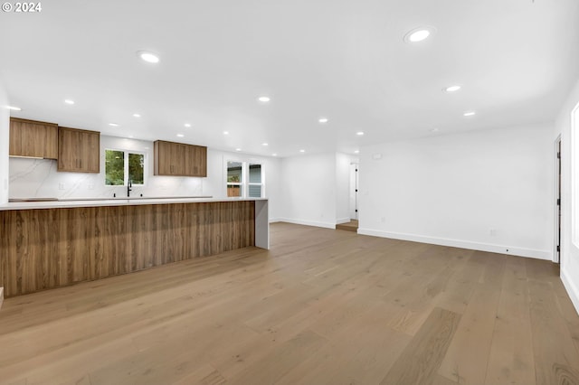 kitchen with sink, light wood-type flooring, backsplash, and kitchen peninsula