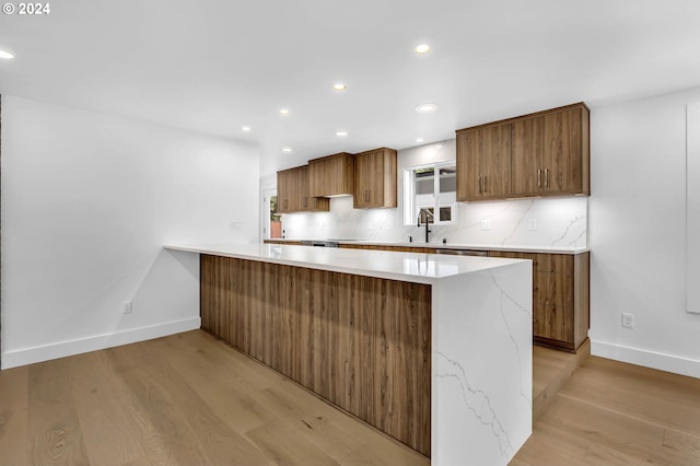 kitchen with light hardwood / wood-style flooring, kitchen peninsula, tasteful backsplash, and sink