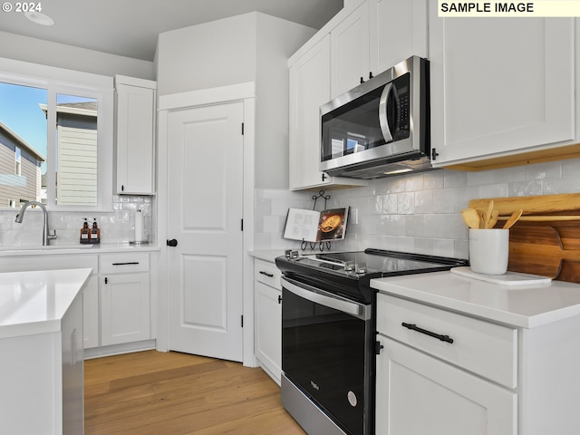 kitchen featuring white cabinets, tasteful backsplash, appliances with stainless steel finishes, light hardwood / wood-style flooring, and sink