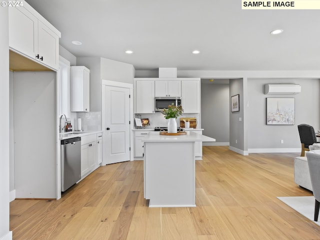 kitchen with a kitchen island, an AC wall unit, stainless steel appliances, light wood-type flooring, and white cabinetry