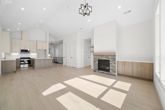 unfurnished living room with high vaulted ceiling, a stone fireplace, sink, light wood-type flooring, and a chandelier