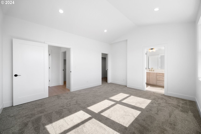 unfurnished bedroom featuring carpet floors, ensuite bathroom, and vaulted ceiling