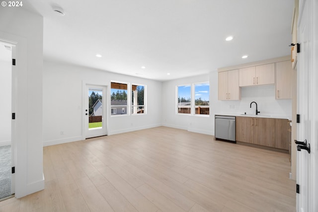 kitchen with light brown cabinetry, light hardwood / wood-style flooring, stainless steel dishwasher, and sink