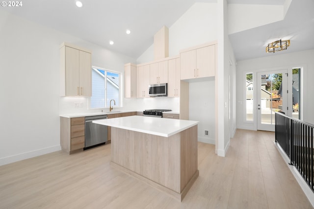 kitchen featuring stainless steel appliances, sink, high vaulted ceiling, a center island, and light hardwood / wood-style floors