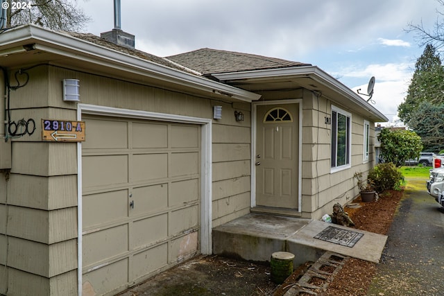 doorway to property featuring a chimney, an attached garage, and roof with shingles