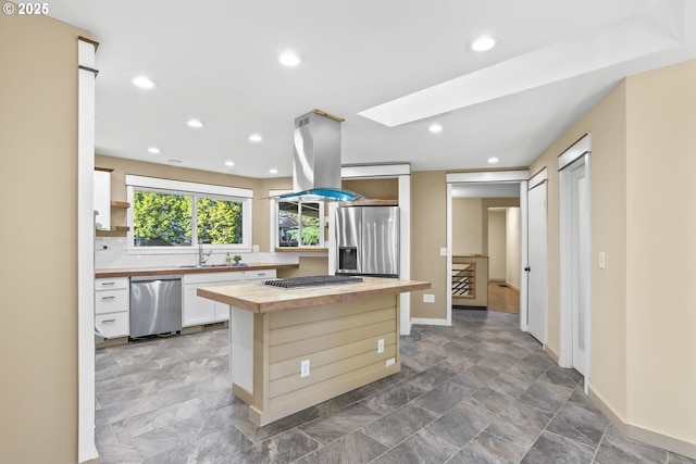 kitchen with stainless steel appliances, butcher block countertops, a skylight, a sink, and island exhaust hood