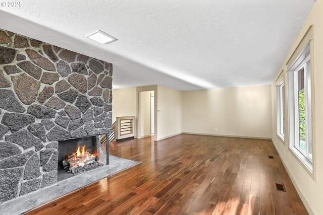 unfurnished living room with visible vents, baseboards, hardwood / wood-style flooring, a textured ceiling, and a fireplace