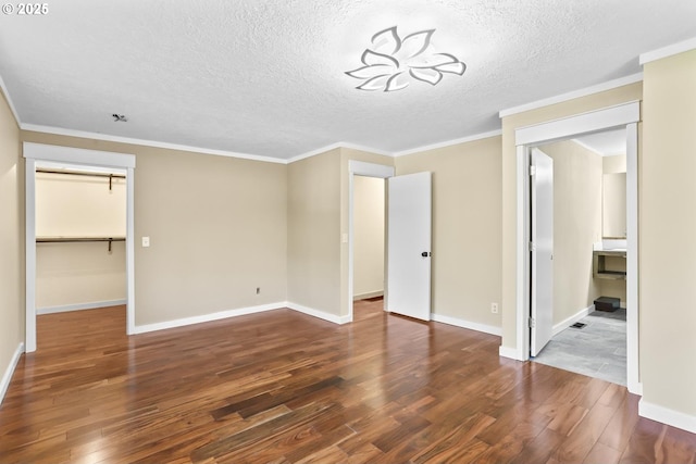 unfurnished bedroom featuring crown molding, baseboards, a walk in closet, and wood finished floors