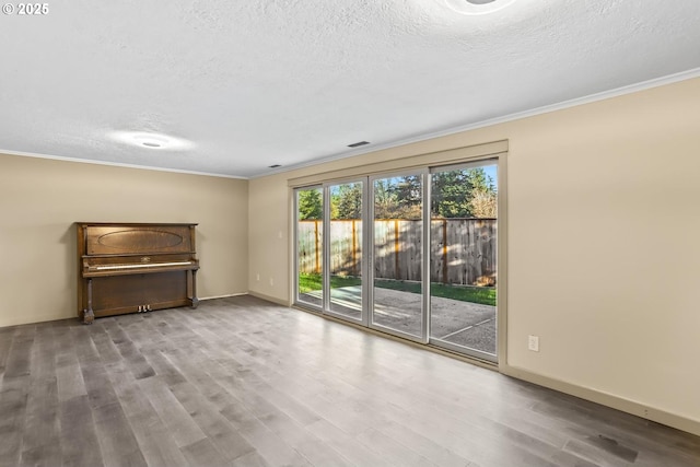 spare room featuring crown molding, a textured ceiling, baseboards, and wood finished floors