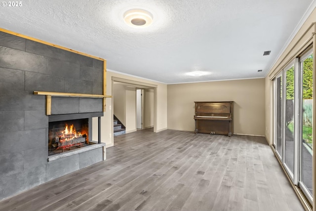 unfurnished living room with crown molding, a tiled fireplace, and wood finished floors