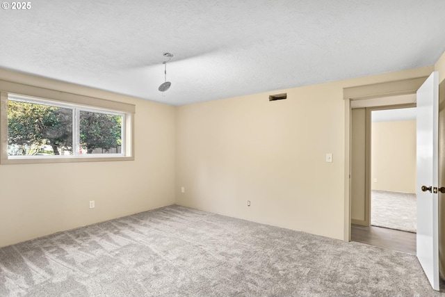 unfurnished room with a textured ceiling, carpet floors, and visible vents