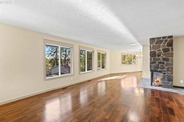 unfurnished living room featuring wood-type flooring, visible vents, a stone fireplace, a textured ceiling, and baseboards