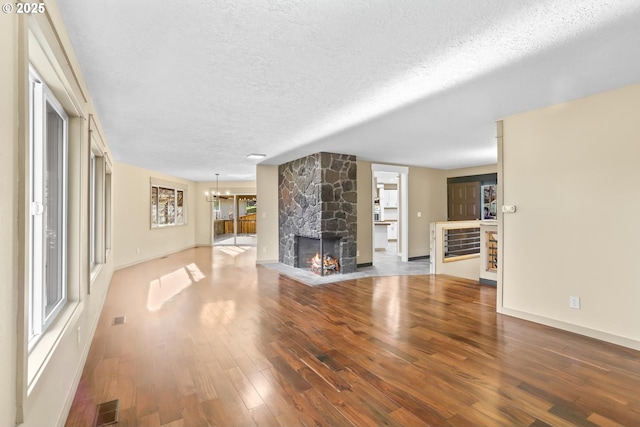 unfurnished living room with visible vents, wood finished floors, an inviting chandelier, a textured ceiling, and a stone fireplace