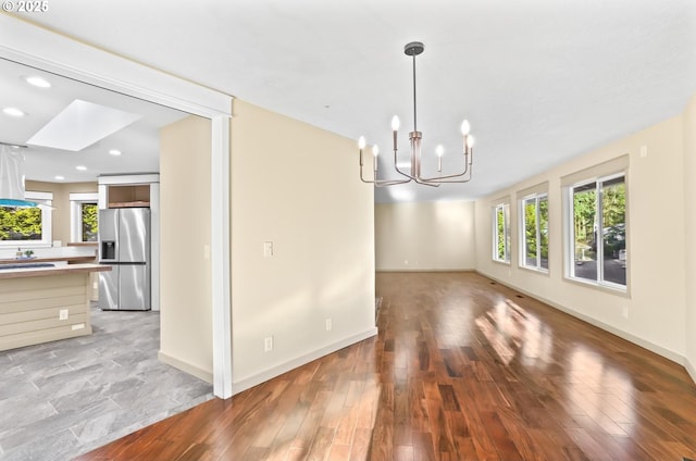 unfurnished dining area featuring baseboards, recessed lighting, light wood-style flooring, and a notable chandelier