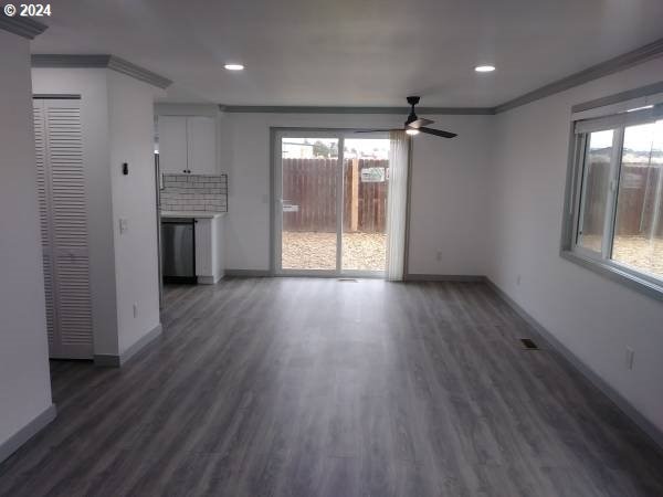 unfurnished living room featuring ornamental molding, a healthy amount of sunlight, ceiling fan, and dark hardwood / wood-style flooring