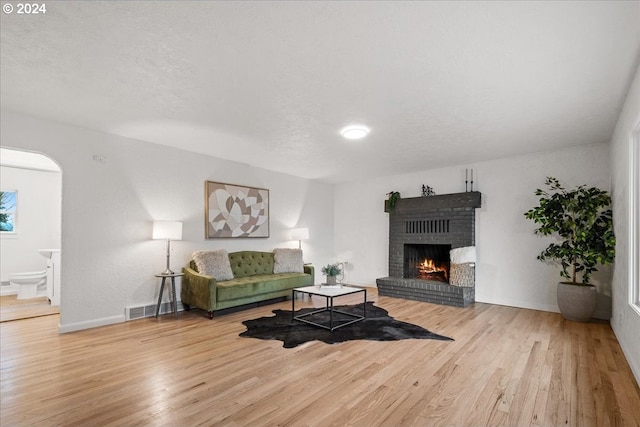 living room with hardwood / wood-style floors, a textured ceiling, and a brick fireplace