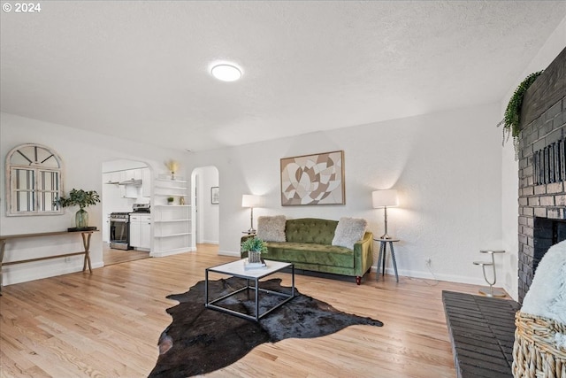 living room featuring a brick fireplace, a textured ceiling, and light hardwood / wood-style flooring