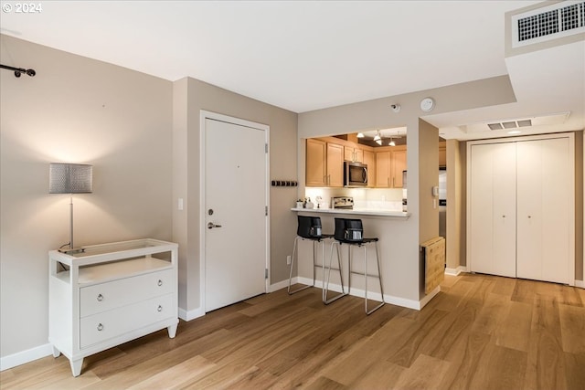 kitchen with light brown cabinets, a kitchen breakfast bar, and light hardwood / wood-style floors