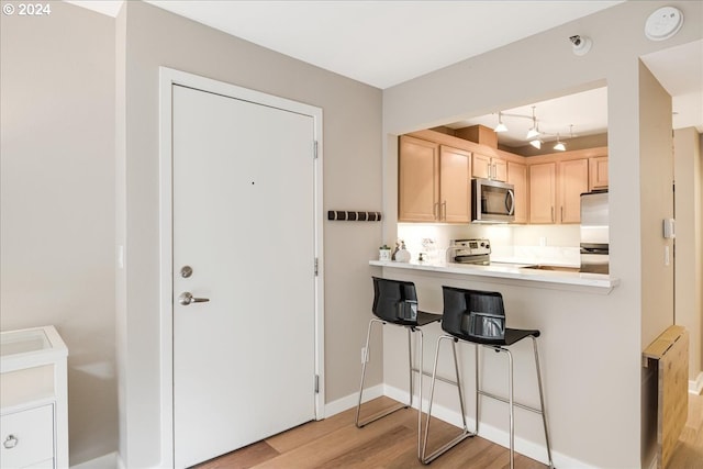 kitchen with light wood-type flooring, appliances with stainless steel finishes, a kitchen bar, light brown cabinetry, and kitchen peninsula