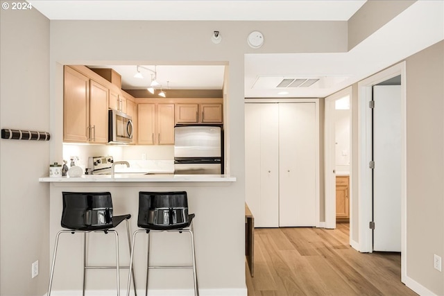 kitchen with kitchen peninsula, stainless steel appliances, light brown cabinetry, and light hardwood / wood-style flooring