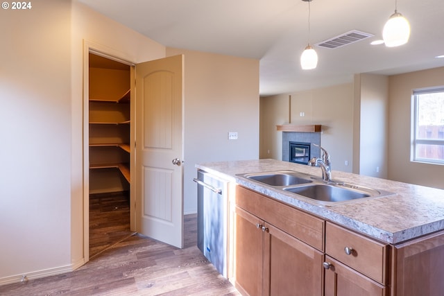 kitchen with pendant lighting, dishwasher, a kitchen island with sink, sink, and light wood-type flooring